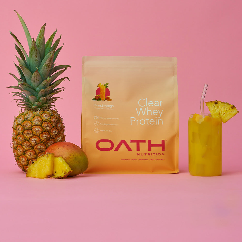 Oath Clear Whey Protein bag next to a pineapple, mango, and glass full of delicious clear whey
