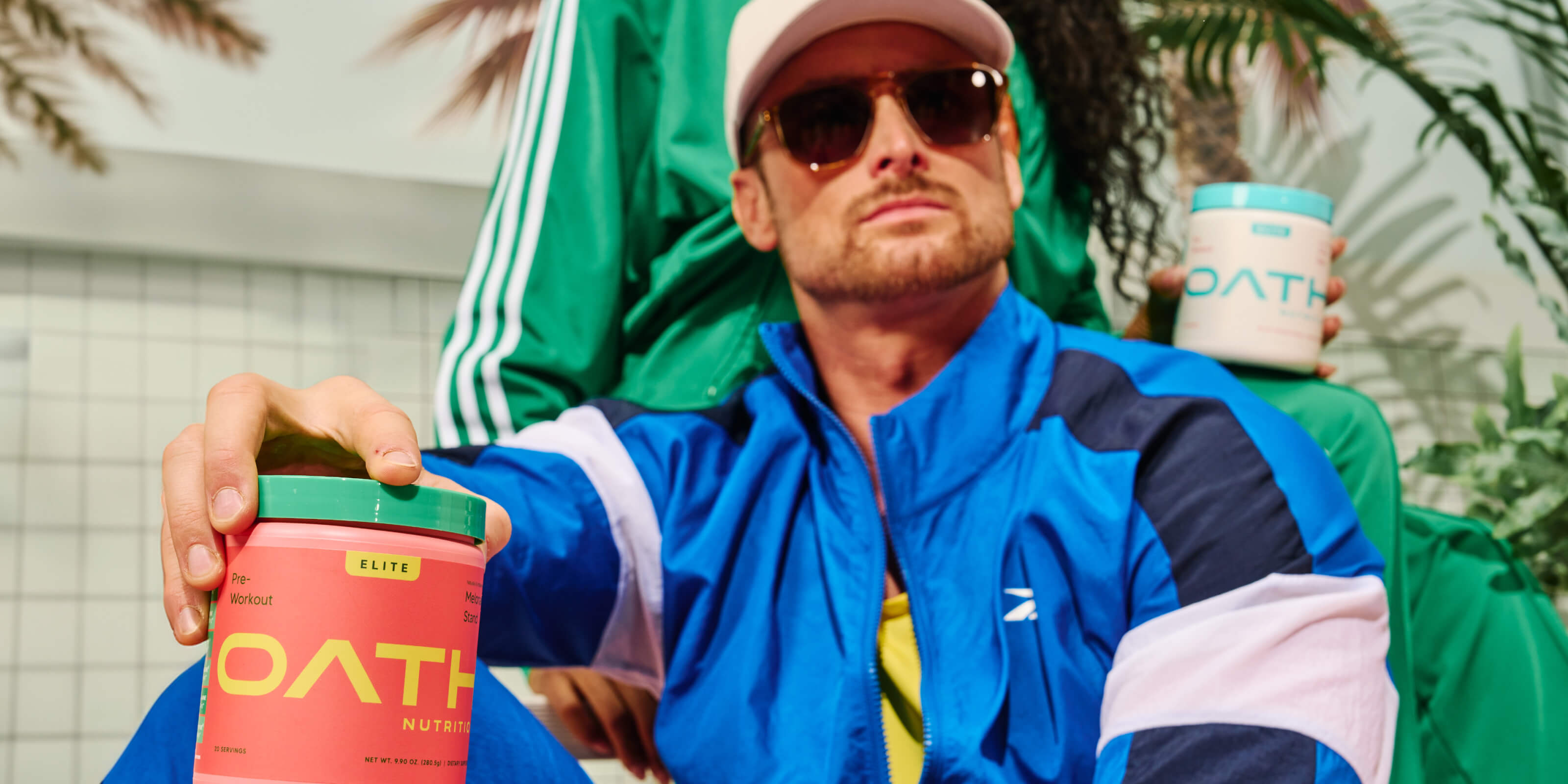 Cool guy holding an Oath Pre-Workout Melonade stand tub with a woman holding a Coco Razz Oath Elite Preworkout tub