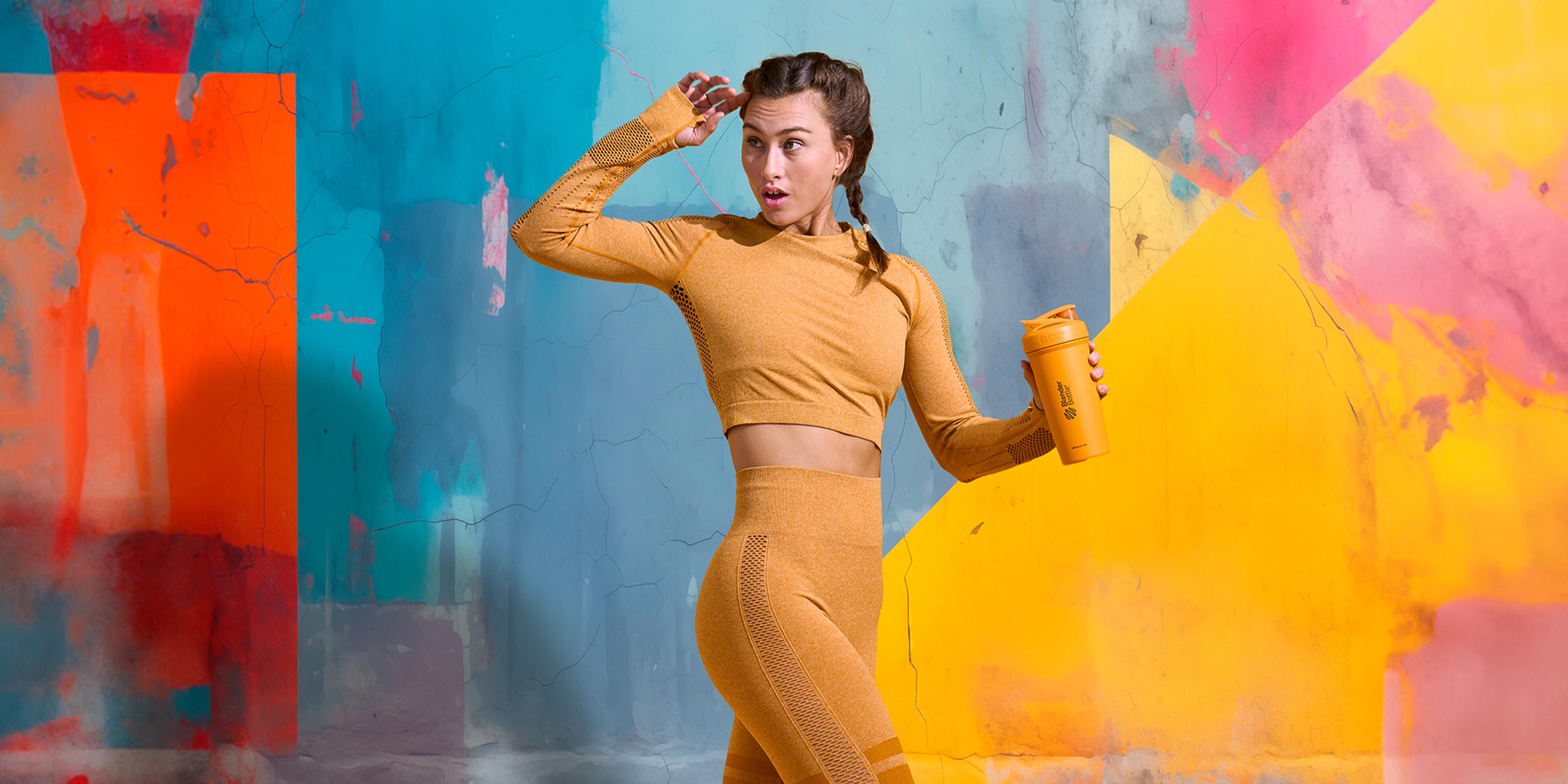 A woman looking to the left during her workout. She is holding a yellow BlenderBottle protein shaker cup in front of a brightly colored background.