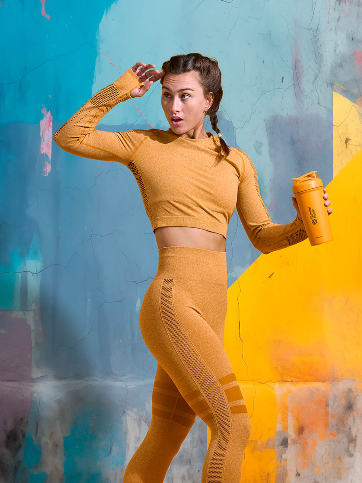 A woman looking to the left during her workout. She is holding a yellow BlenderBottle protein shaker cup in front of a brightly colored background.