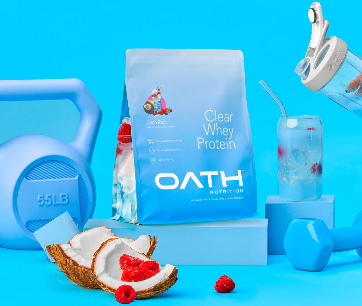 Oath Clear Whey Protein Coco Razz bag sitting in the middle of gym equipment. A BlenderBottle shaker bottle pours protein into a glass on the right side.