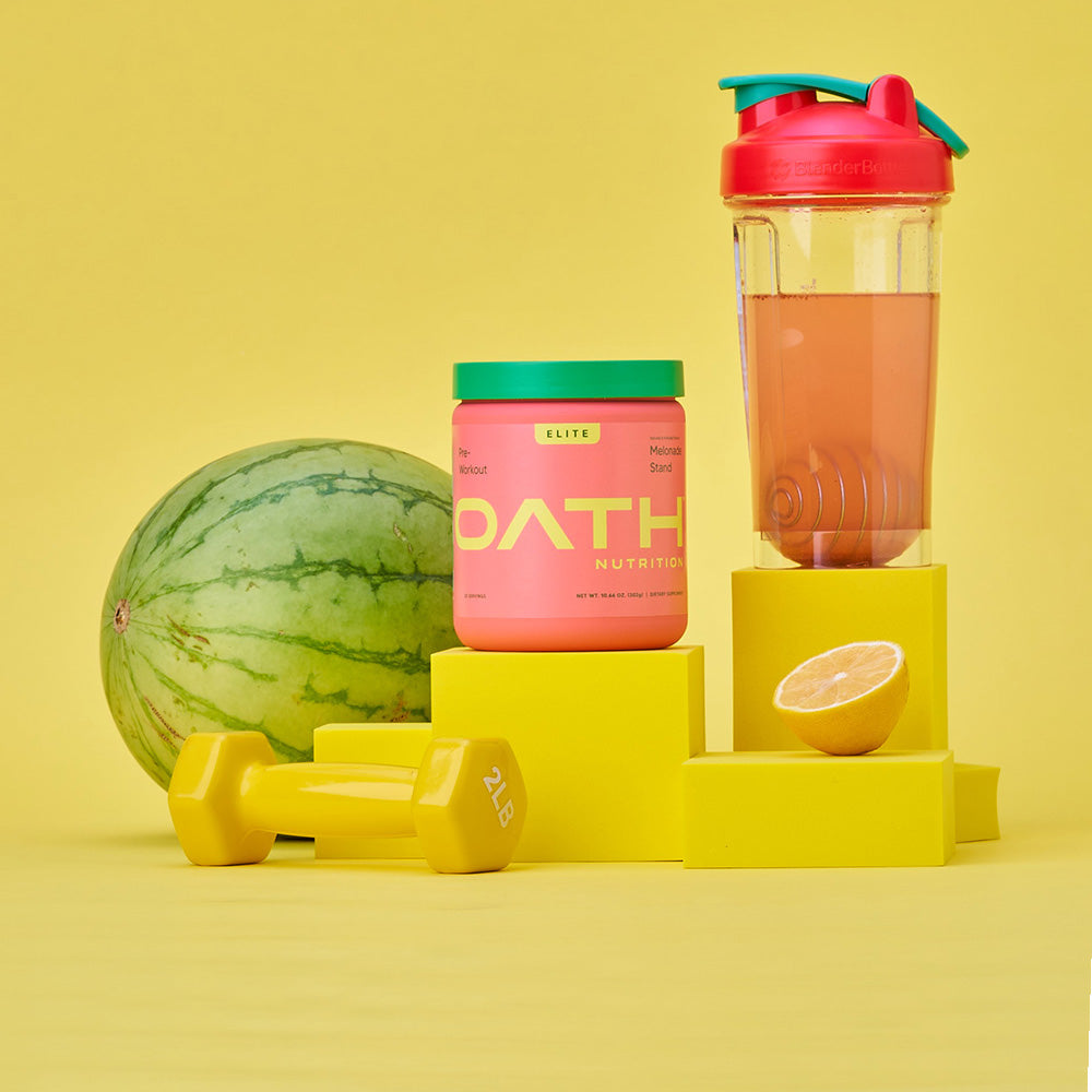 Oath Pre-Workout Melonade Stand container on a stand with a watermelon, weight, lemon, and BlenderBottle brand shaker bottle in the background