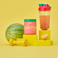 Oath Pre-Workout Melonade Stand container on a stand with a watermelon, weight, lemon, and BlenderBottle brand shaker bottle in the background