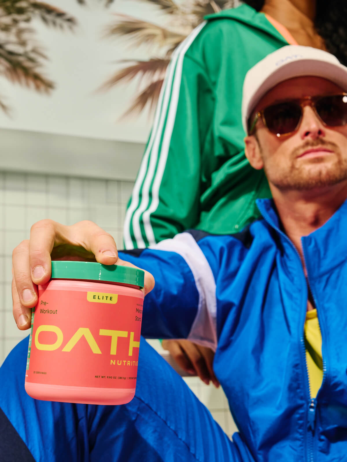 Cool guy holding an Oath Pre-Workout Melonade stand tub with a woman holding a Coco Razz Oath Elite Preworkout tub
