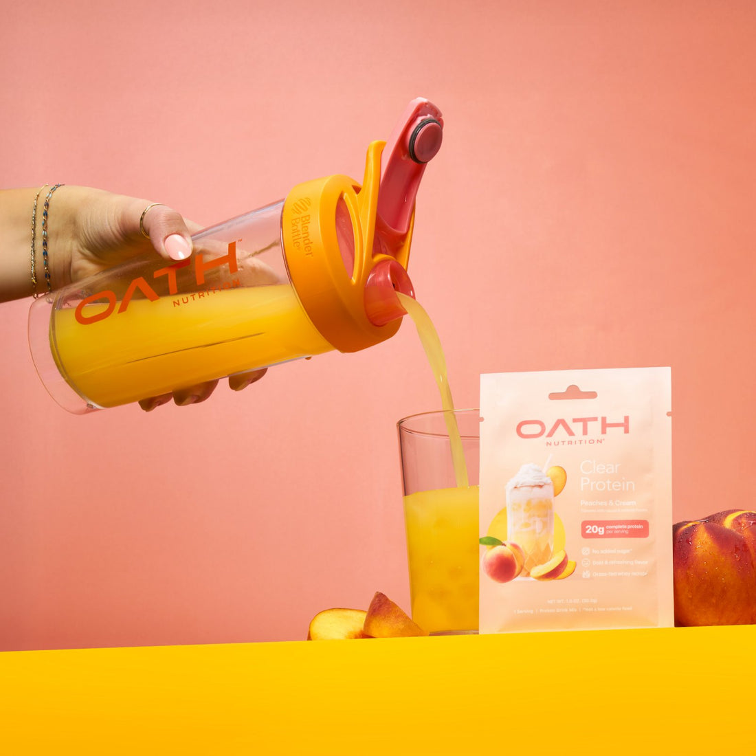 A hand pours orange juice from a clear OATH-branded bottle into a glass. An OATH Clear Protein powder packet stands next to the glass with peaches visible.